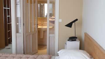 A bedroom with a bed, a bedside table with a lamp, a wardrobe, and a bathroom visible through an open door.