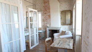 A rustic room with a wooden floor, white furniture, a fireplace, and a large mirror on the wall. - Hôtel Le Sénéchal (Ars-en-Re)