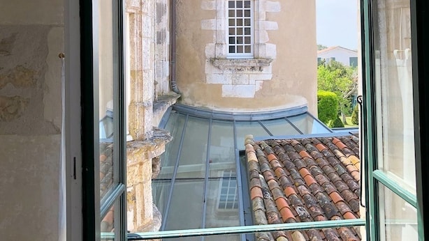 A view from a balcony with a glass floor, looking at a building with a tiled roof and a small window. - Hôtel Le Sénéchal (Ars-en-Re)