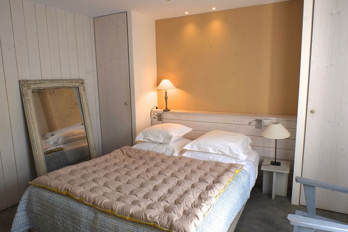 Een slaapkamer met een bed, twee bedlampen, een spiegel en een houten bankje.