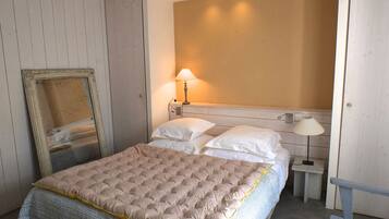 Een slaapkamer met een bed, twee bedlampen, een spiegel en een houten bankje.