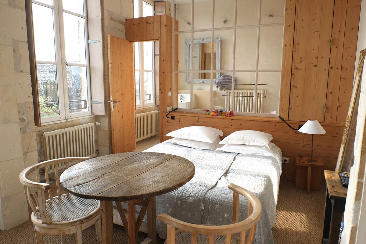 Una habitación con una cama de madera, una mesa redonda, dos sillas, un espejo y un radiador.