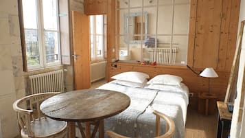 Una habitación con una cama de madera, una mesa redonda, dos sillas, un espejo y un radiador.