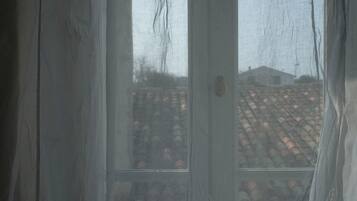 A view through a window with a metal grid, a door with a brass handle, and a tiled roof visible outside.