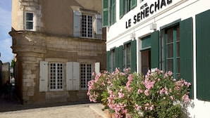 A hotel named "Le Senchal" with a cobblestone street, green shutters, and potted pink flowers in front. - Hôtel Le Sénéchal (Ars-en-Re)