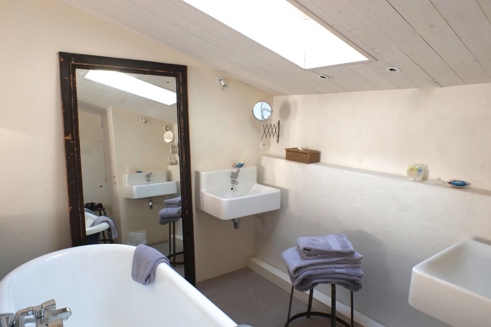 A bathroom with a skylight, two sinks, a large mirror, and a bathtub.
