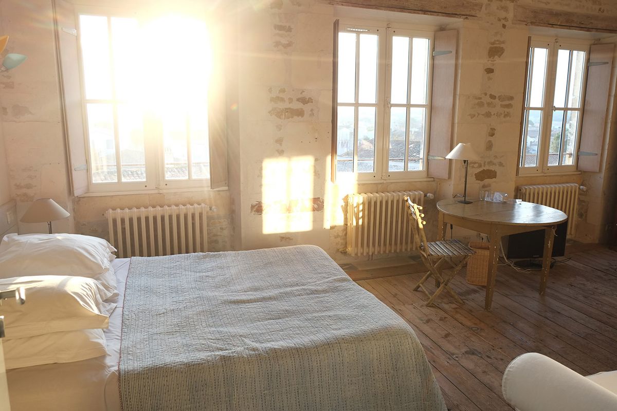 Una habitación con cama, escritorio y silla. Amplios ventanales permiten la entrada de luz natural.