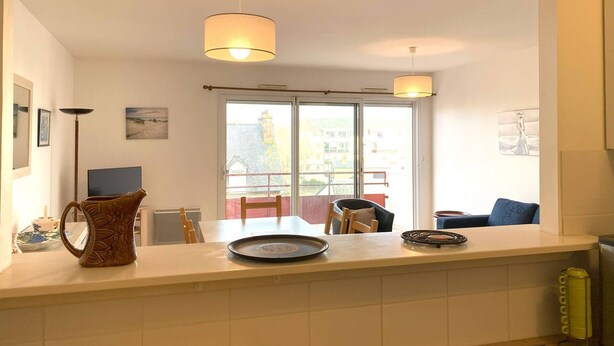 A modern kitchen with a large window, a dining area with chairs, and a coffee table. - Spacious apartment with WIFI, 2 bedrooms, downtown Perros-Guirec, near beaches (Perros-Guirec)