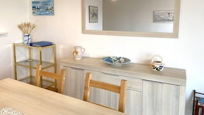 A dining area with a wooden table, chairs, a glass-top table, and a light-colored cabinet with decorative items. - Spacious apartment with WIFI, 2 bedrooms, downtown Perros-Guirec, near beaches (Perros-Guirec)