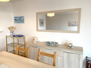 A dining area with a wooden table, chairs, a glass-top table, and a light-colored cabinet with decorative items. - Spacious apartment with WIFI, 2 bedrooms, downtown Perros-Guirec, near beaches (Perros-Guirec)