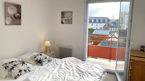 A bedroom with a bed, a nightstand with a lamp, and a sliding glass door leading to a balcony. - Spacious apartment with WIFI, 2 bedrooms, downtown Perros-Guirec, near beaches (Perros-Guirec)