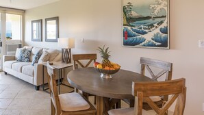 Un coin repas avec une table ronde, des chaises en bois, un saladier de fruits, un canapé et un tableau accroché au mur.