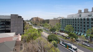 A cityscape with modern buildings, a clear sky, and a street with cars and a bus.
