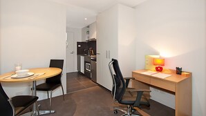 A modern hotel room with a dining area, a workspace, and a kitchenette.