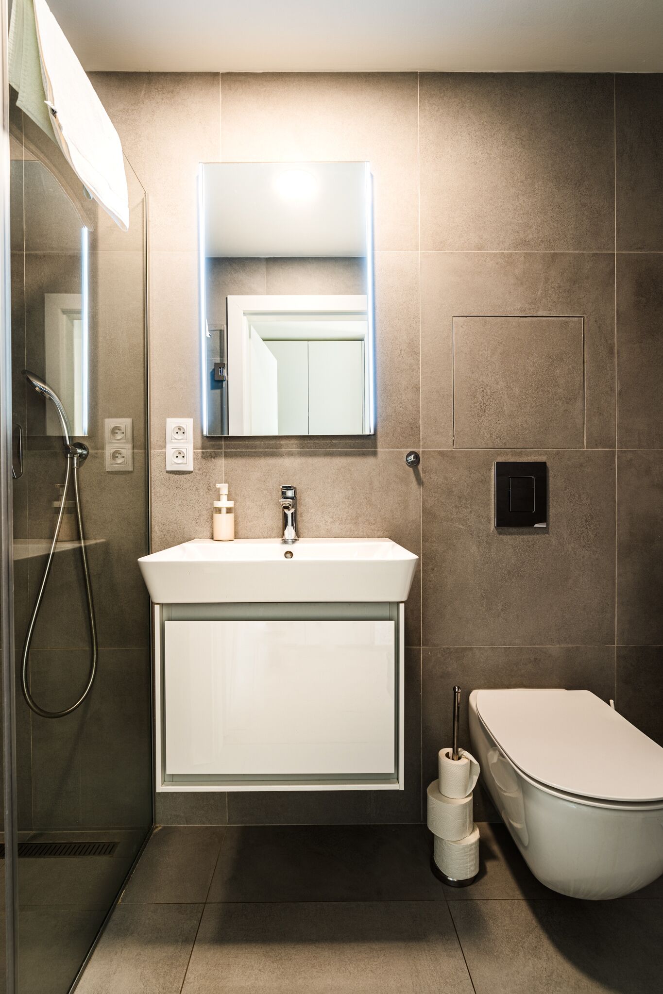 A modern bathroom with a shower, sink, toilet, and a mirror above the sink.