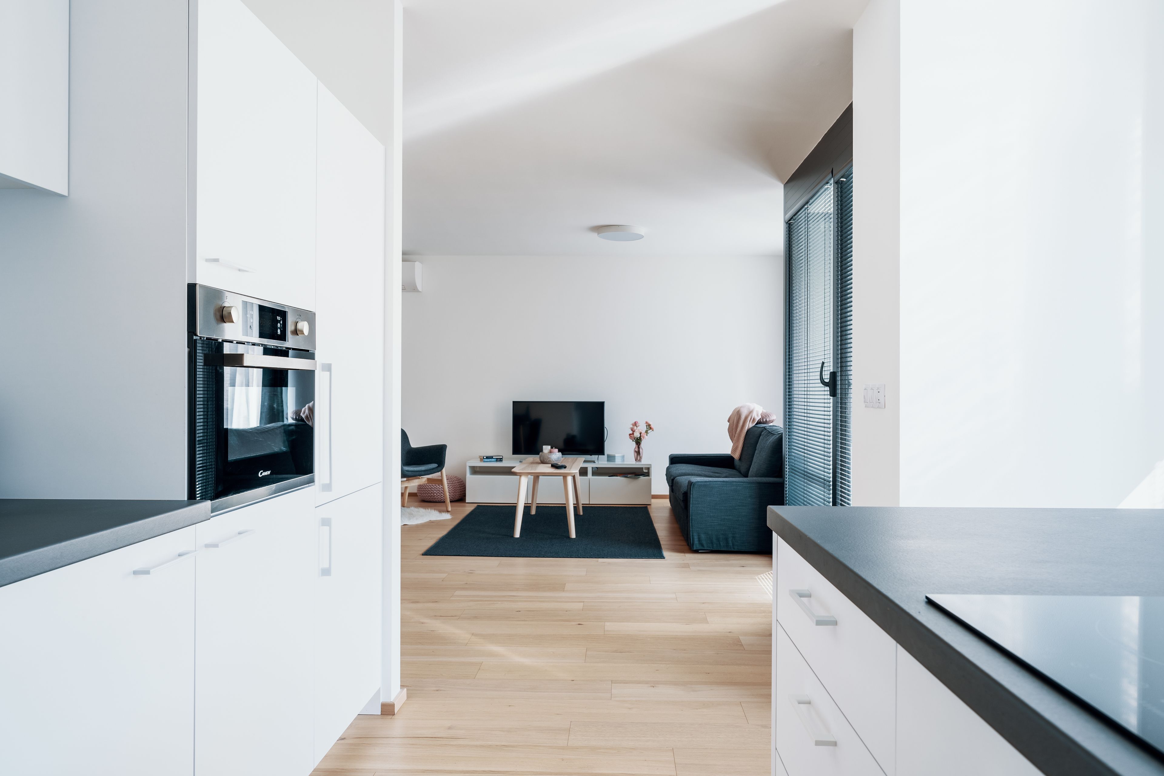 A modern kitchen with built-in appliances, a dining area with a table and chairs, and a living room with a sofa and a TV.