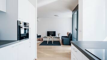 A modern kitchen with built-in appliances, a dining area with a table and chairs, and a living room with a sofa and a TV.