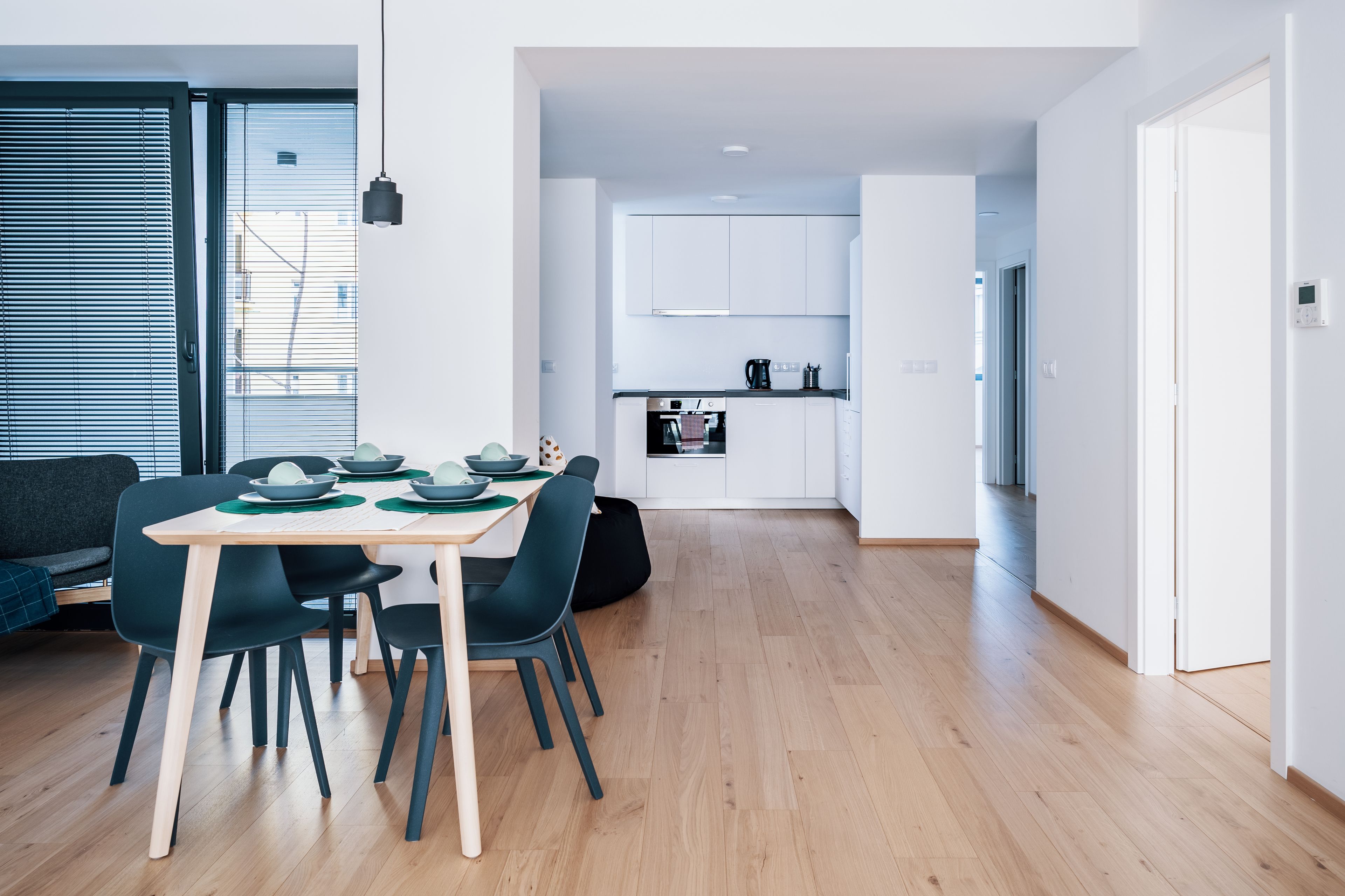 A modern kitchen with white cabinets, a dining area with a wooden table and chairs, and a view of the city through large windows.