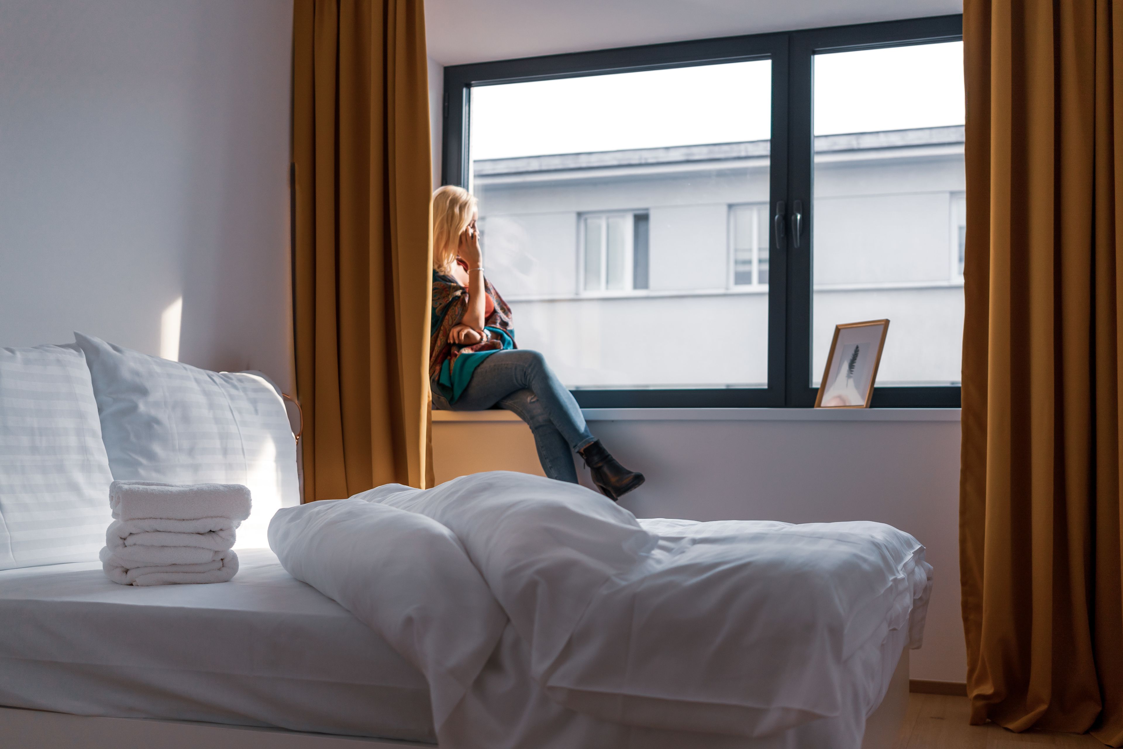 A hotel room with a bed, a window with curtains, and a view of buildings outside.
