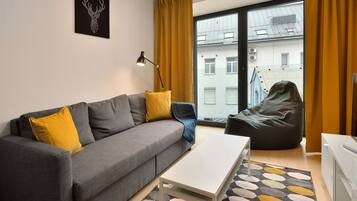 Een moderne woonkamer met een grijze bank, gele kussens, een witte salontafel, een relaxfauteuil en een groot raam met gele gordijnen.