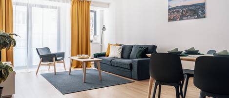 A modern living room with a sofa, chairs, a dining table, and a large window with curtains.