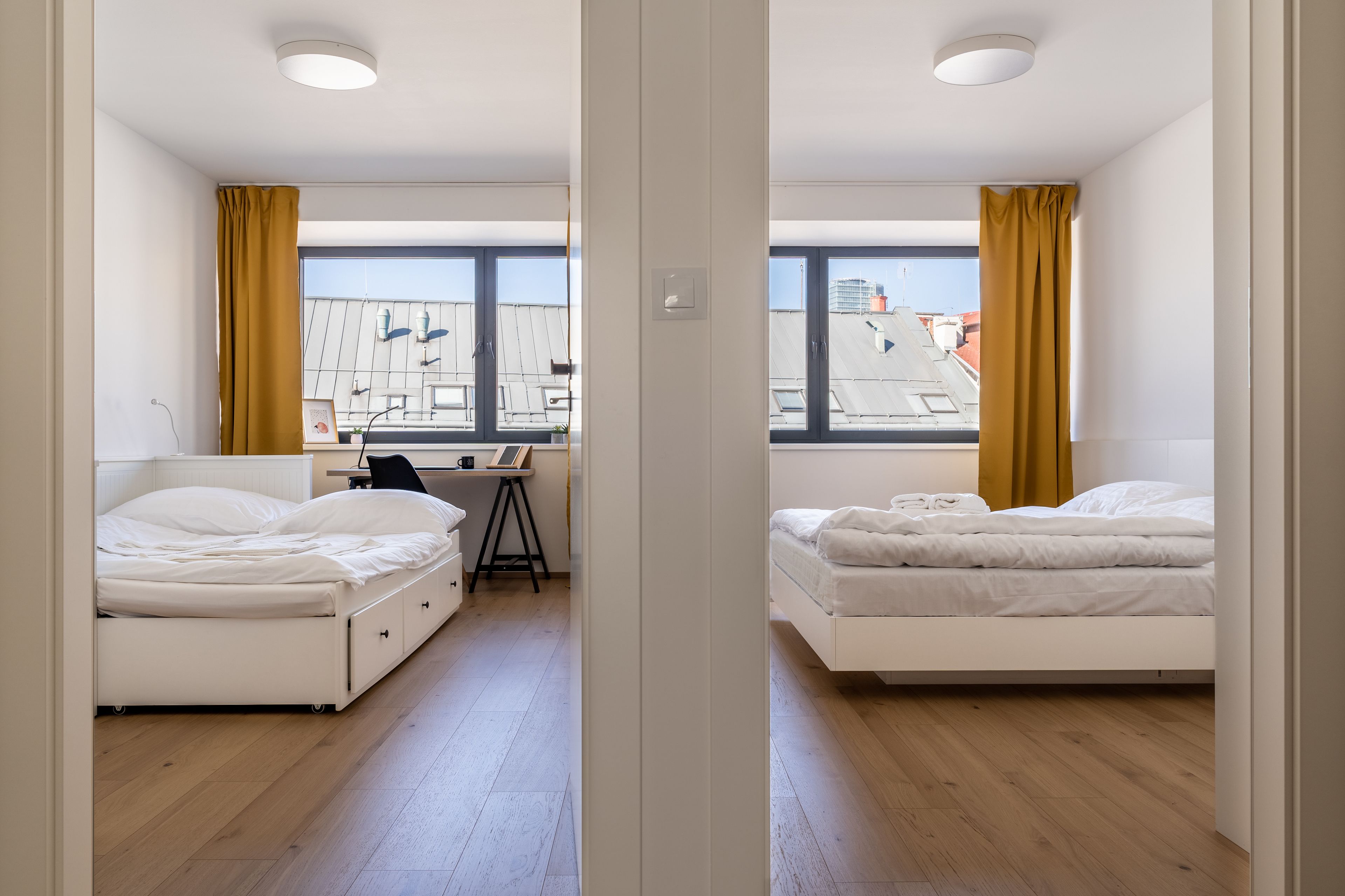 Ett modernt hotellrum med två sängar, ett skrivbord och stora fönster med gardiner.