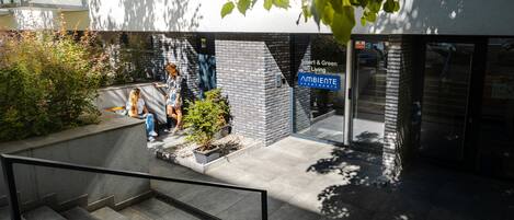Un edificio moderno con fachada de ladrillo, un pequeño jardín y un letrero que dice 'Smart & Green Living Apartments'.
