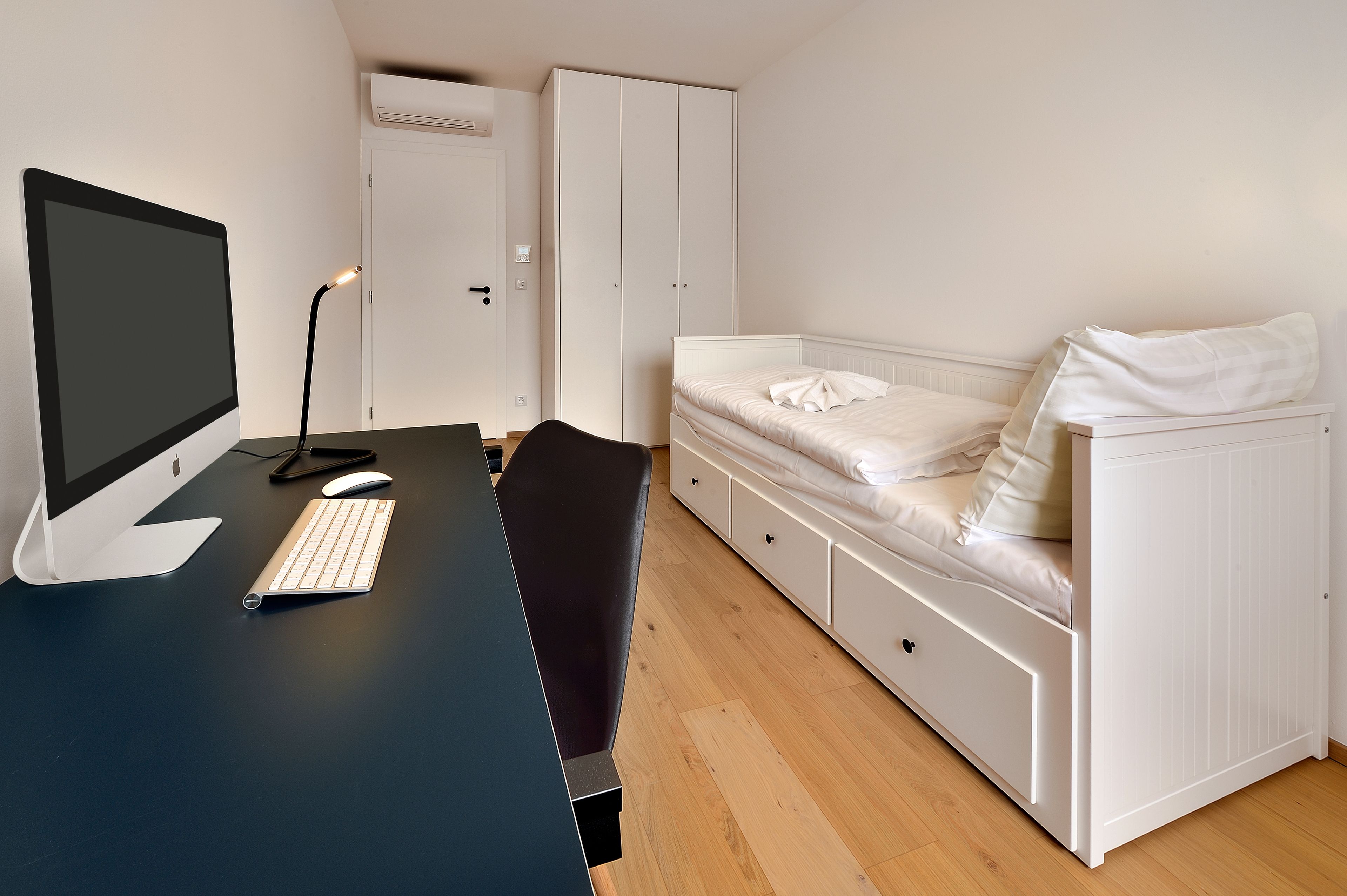 A bedroom with a desk, computer, and bed.