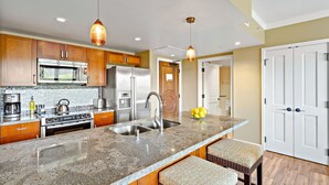 A modern kitchen with granite countertops, stainless steel appliances, and wooden cabinets. - Maui Resort Rentals: Honua Kai Konea 438 – Luxurious 1BR Suite w/ Upgraded Interior and Tranquil, Private Location (Lahaina)