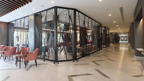 A modern hotel lobby with a geometric partition, seating areas, and a visible staircase.