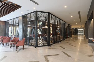 Un moderno vestíbulo de hotel con un separador geométrico, zonas de estar y una escalera visible.