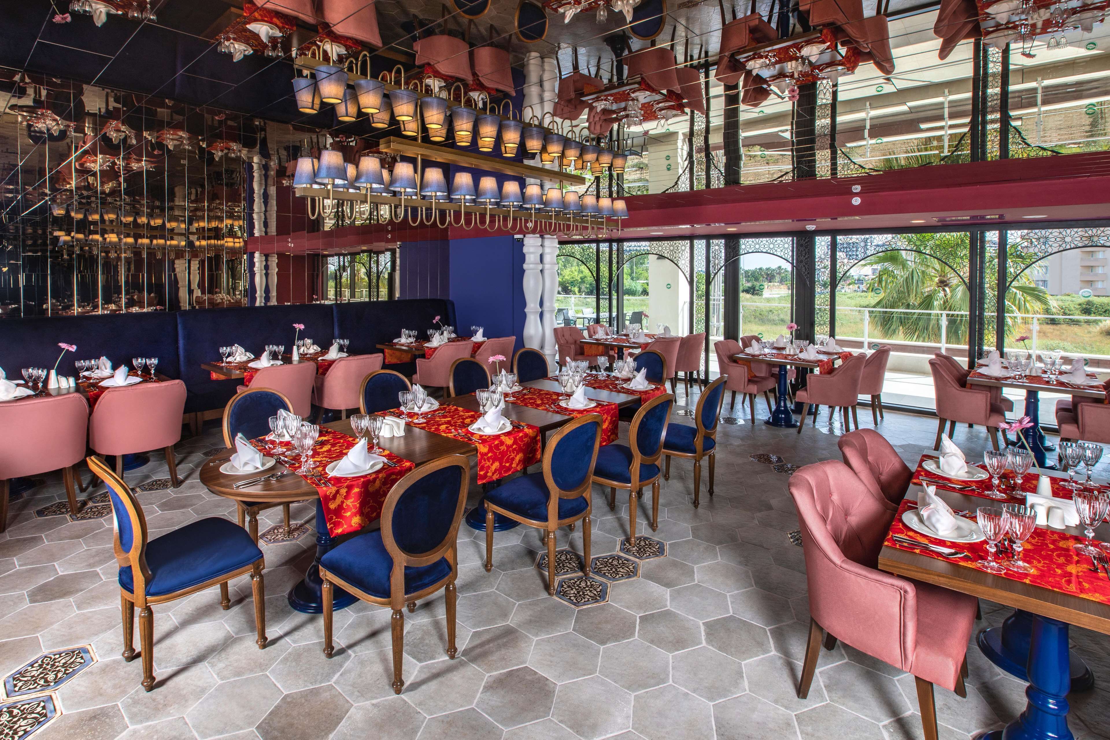 Ein Restaurant mit sechseckigem Fliesenboden, rot- und blaubezogenen Stühlen sowie Tischen, die mit weißen Tischdecken und Besteck gedeckt sind.