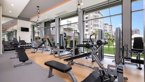 A modern gym with various exercise equipment, large windows, and a view of residential buildings.