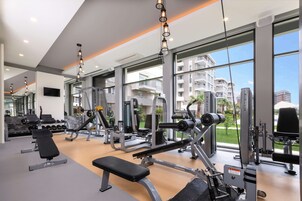 Un gimnasio moderno con diversos equipos de ejercicio, ventanas amplias y vistas a edificios residenciales.