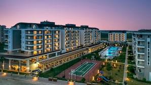 A modern hotel complex with multiple high-rise buildings, a swimming pool, and a tennis court.