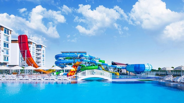 A water park with a large pool, a red water slide, and a multi-level water slide structure.