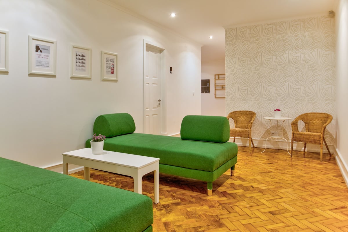 Une pièce avec des canapés verts, une table blanche, des chaises en osier et un mur orné de motifs.