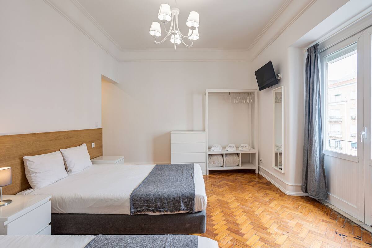 Une chambre d’hôtel avec un grand lit, une armoire, un téléviseur fixé au mur et une fenêtre avec des rideaux.