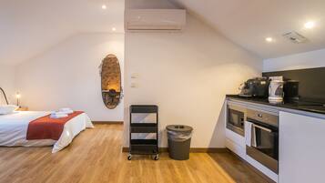 Quarto de hotel com cama, pequena cozinha, lixeira e prateleira fixada na parede.