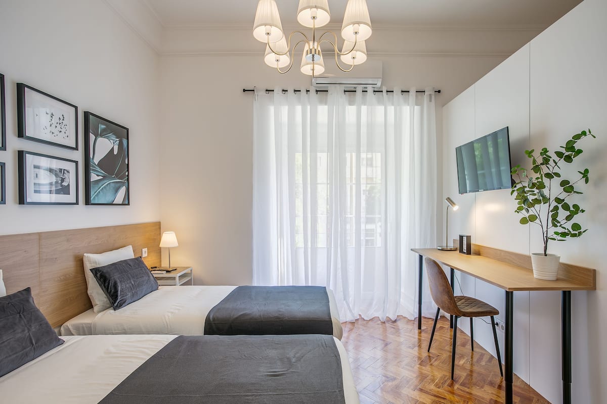Une chambre d’hôtel moderne, équipée de deux lits, d’un bureau, d’une chaise, d’une plante en pot et d’œuvres d’art accrochées aux murs.