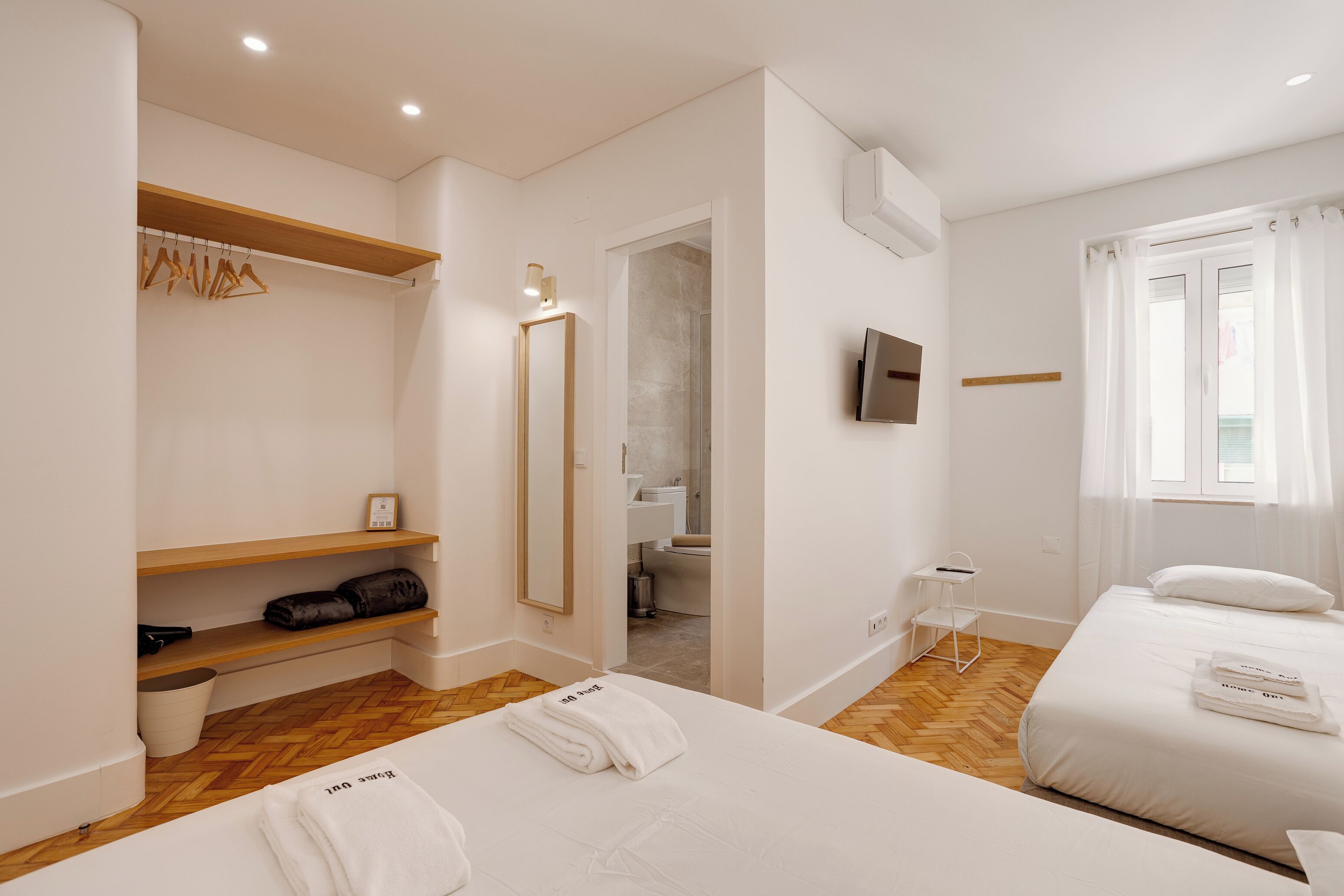 Ett hotellrum med en säng, en garderob, en spegel, en tv och ett badrum som syns genom en öppen dörr.