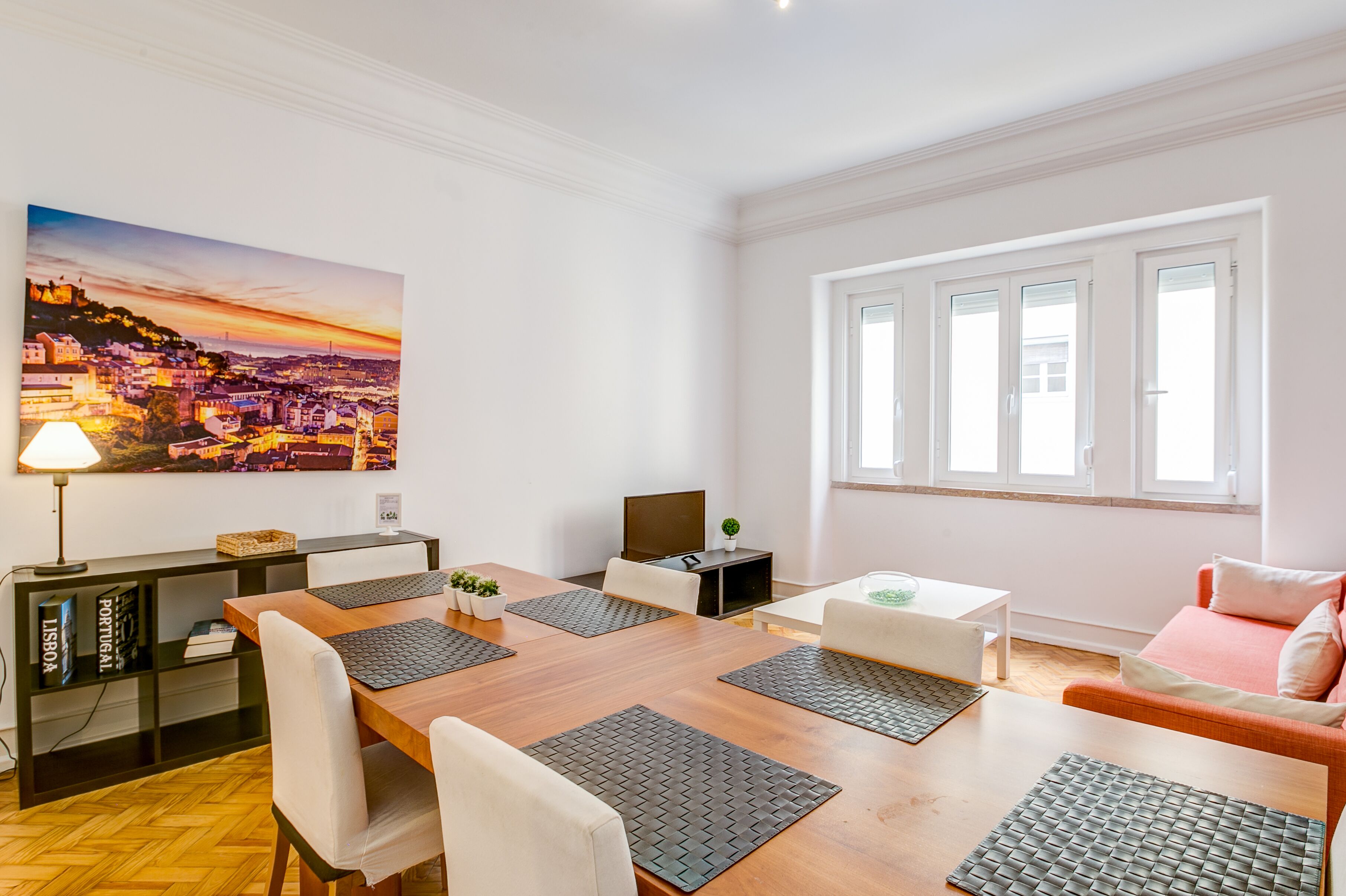 A modern living room with a wooden dining table, white sofas, and a large cityscape painting on the wall.
