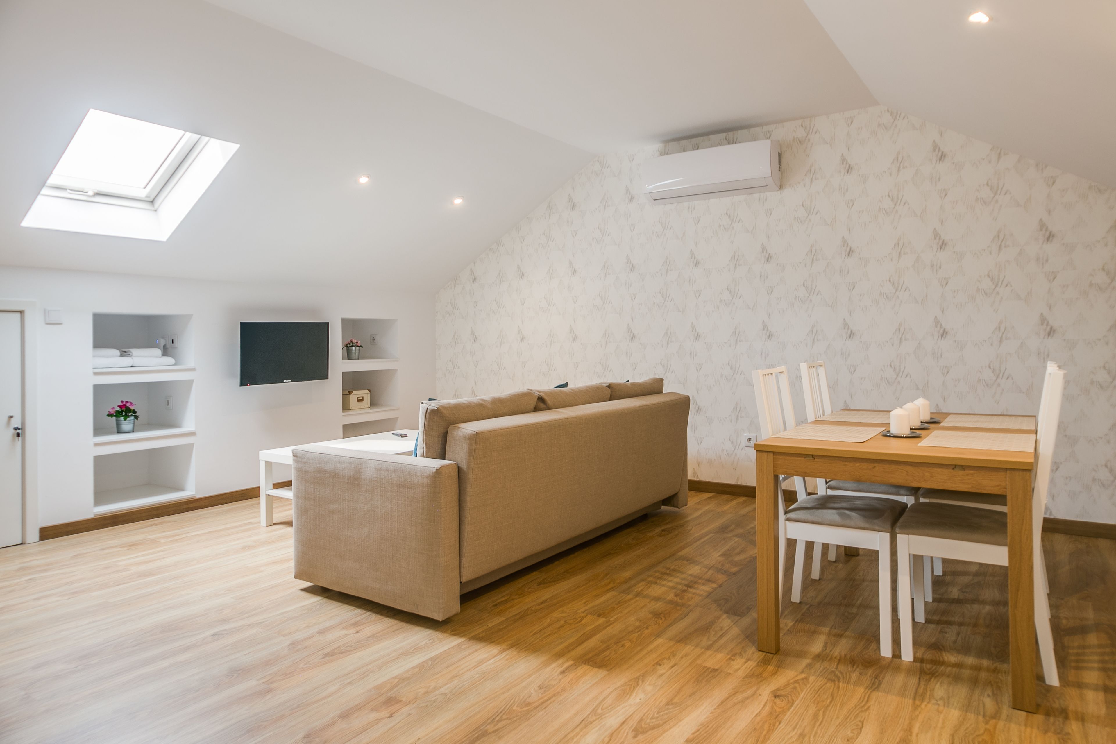 Una sala moderna con un sofá, una mesa de comedor con sillas, un tragaluz y estanterías empotradas.