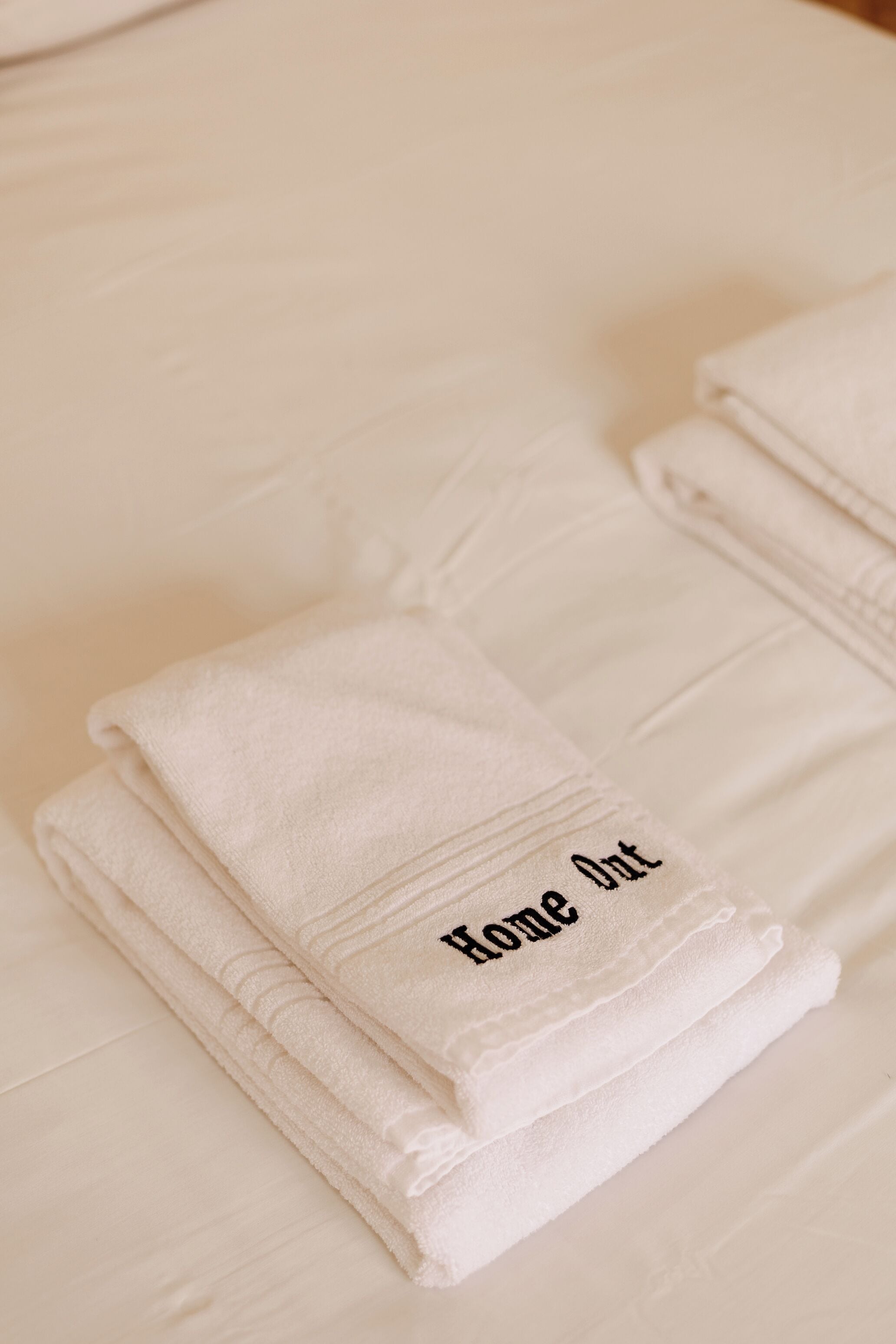 Toallas blancas dobladas cuidadosamente sobre una superficie blanca, con el texto 'Home Out'.