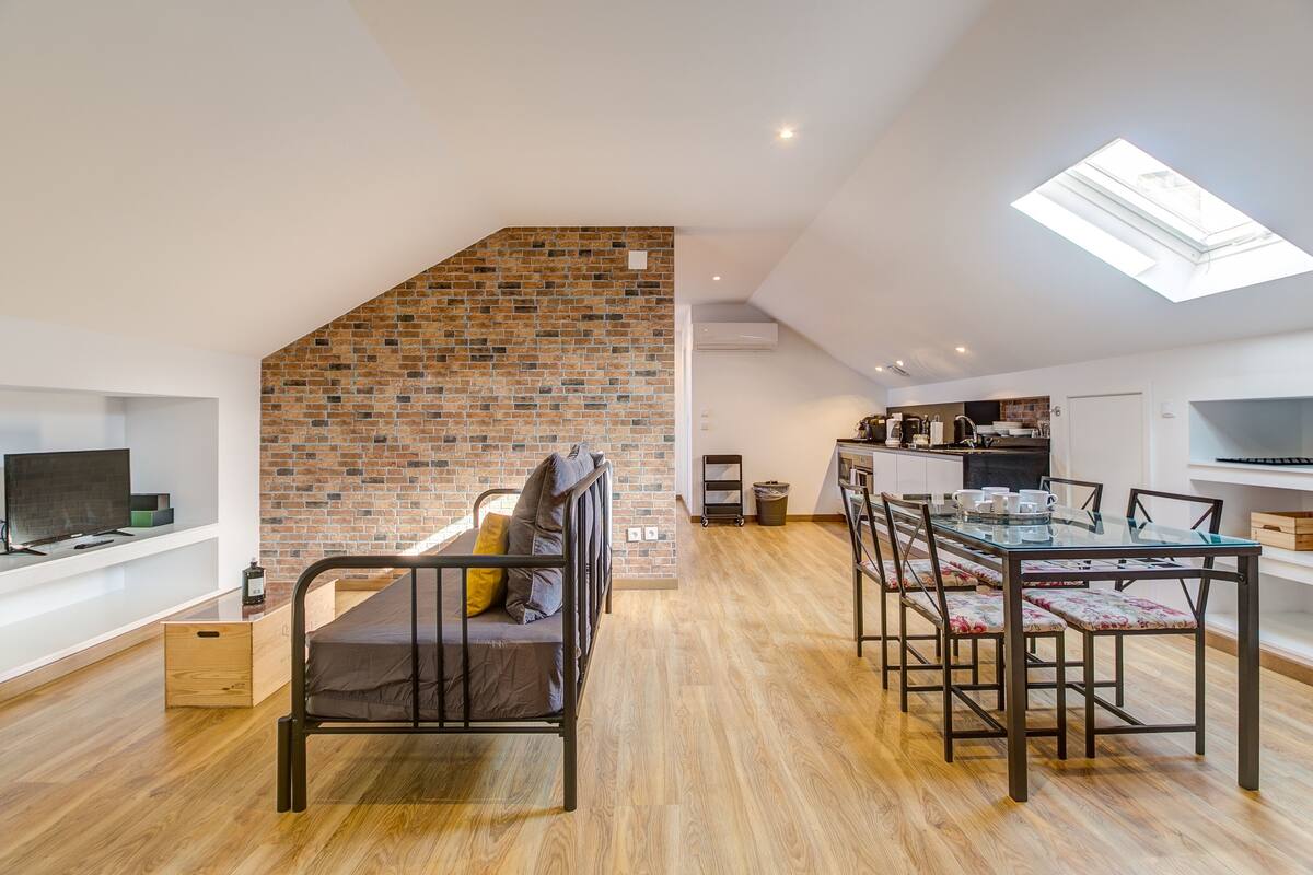 Un appartement moderne de style « loft », avec un lit en mezzanine, un coin repas, une cuisine et un téléviseur situé à gauche.
