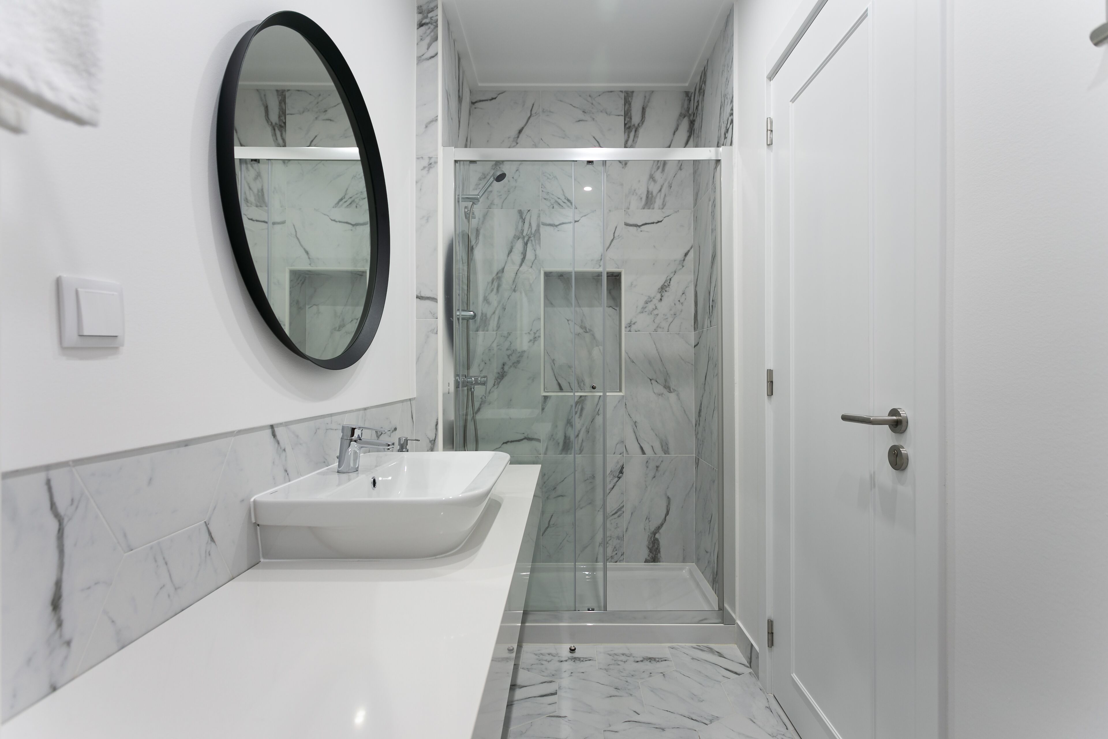 A modern bathroom with a white sink, a large mirror, and a glass-enclosed shower.