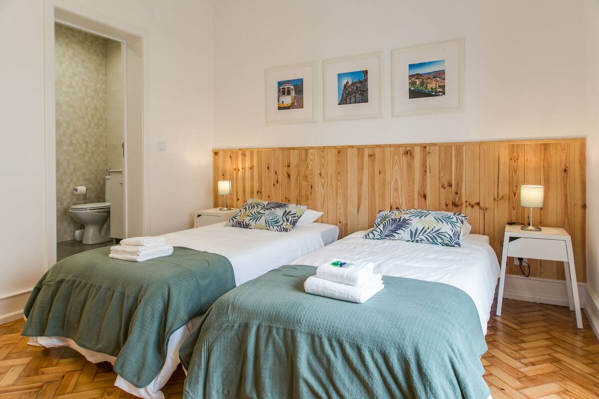 Une chambre d’hôtel avec deux lits, une tête de lit en bois, une petite table de chevet avec une lampe et un mur orné de trois tableaux encadrés.