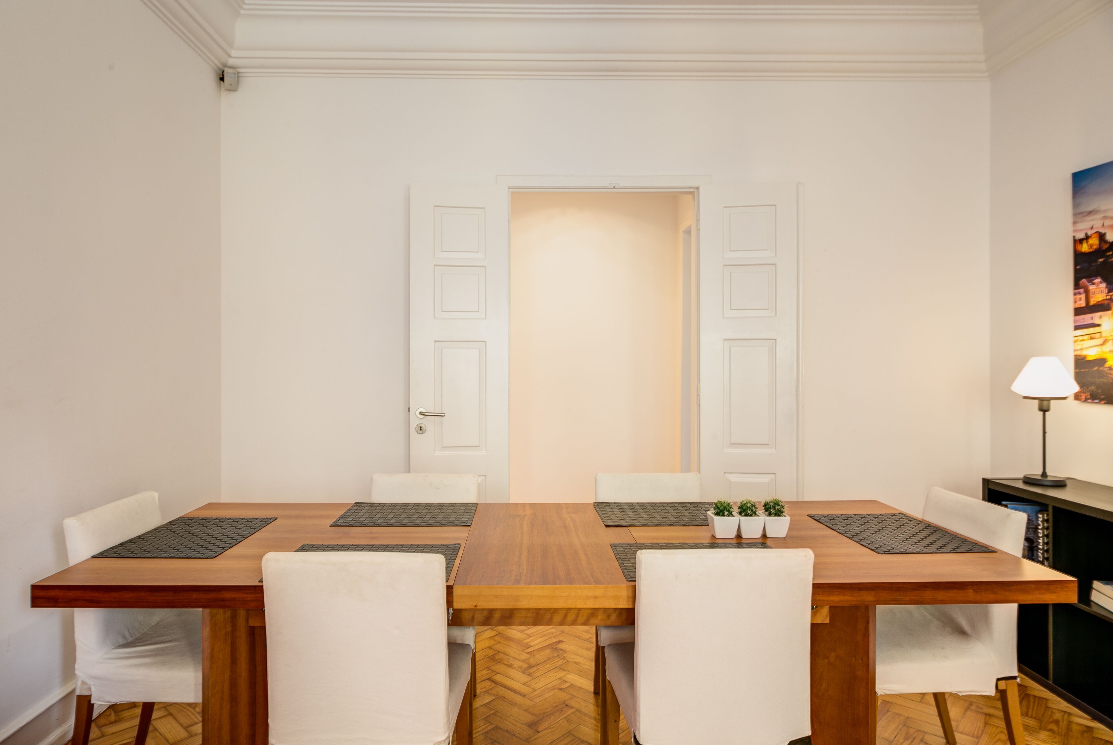 A dining area with a wooden table, white chairs, and a door in the background.