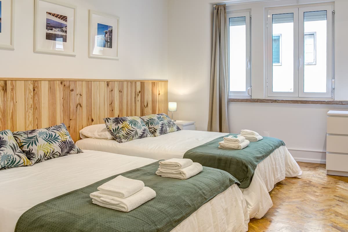 Une chambre d’hôtel avec deux lits, une tête de lit en bois, des couvre-lits verts, des oreillers blancs et une fenêtre avec des rideaux.