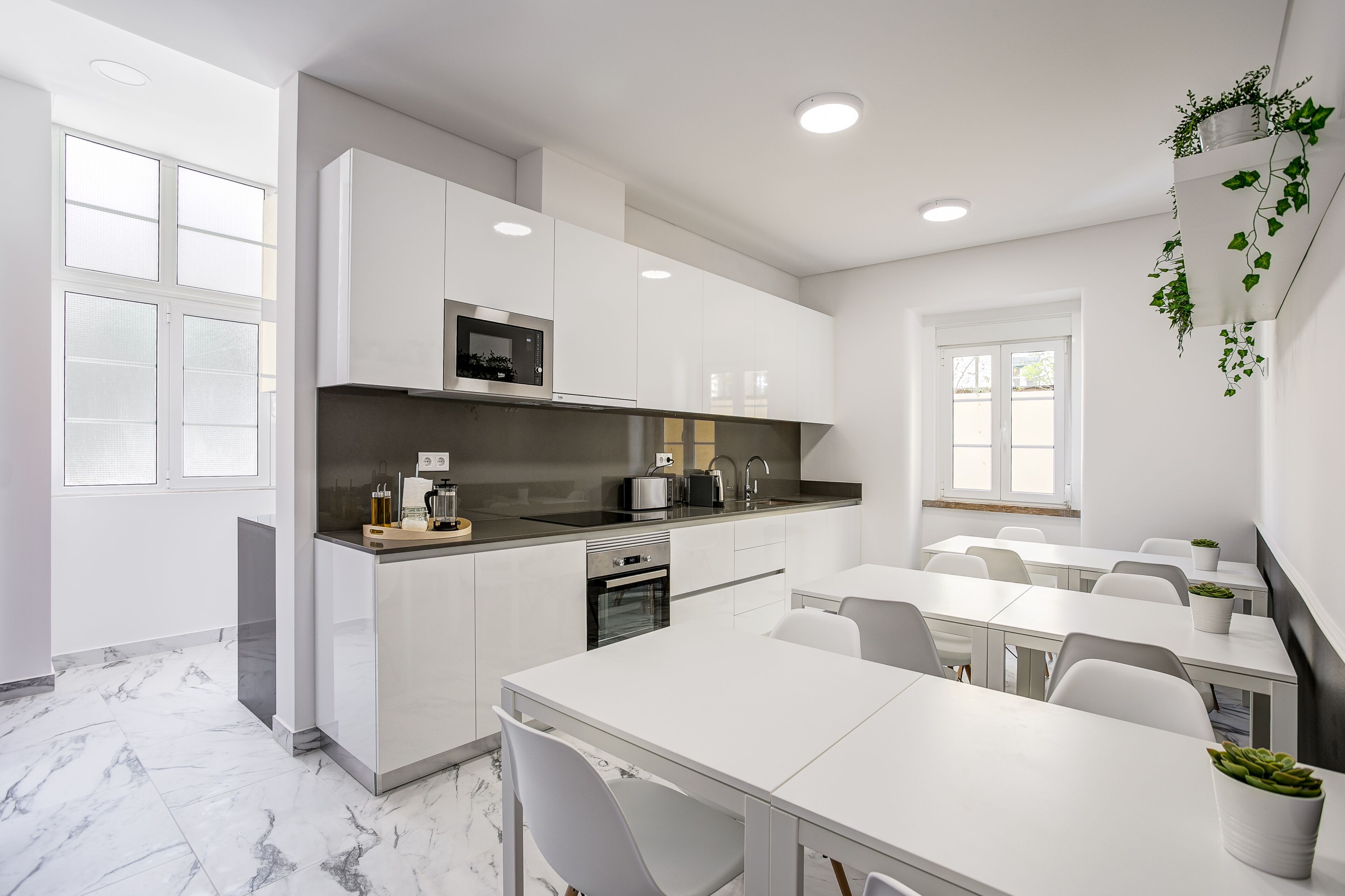 Una cocina moderna con armarios blancos, microondas integrado y un fregadero. Hay sillas blancas y una mesa, y una ventana con vistas.